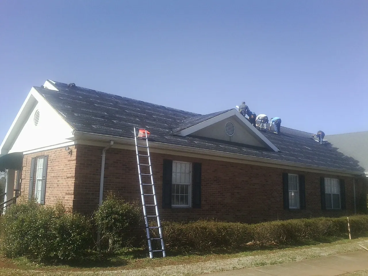 Crew tearing shingles off a brick ranch roof with a ladder set — Emergency Roof Repair work by our crew in Saint George
