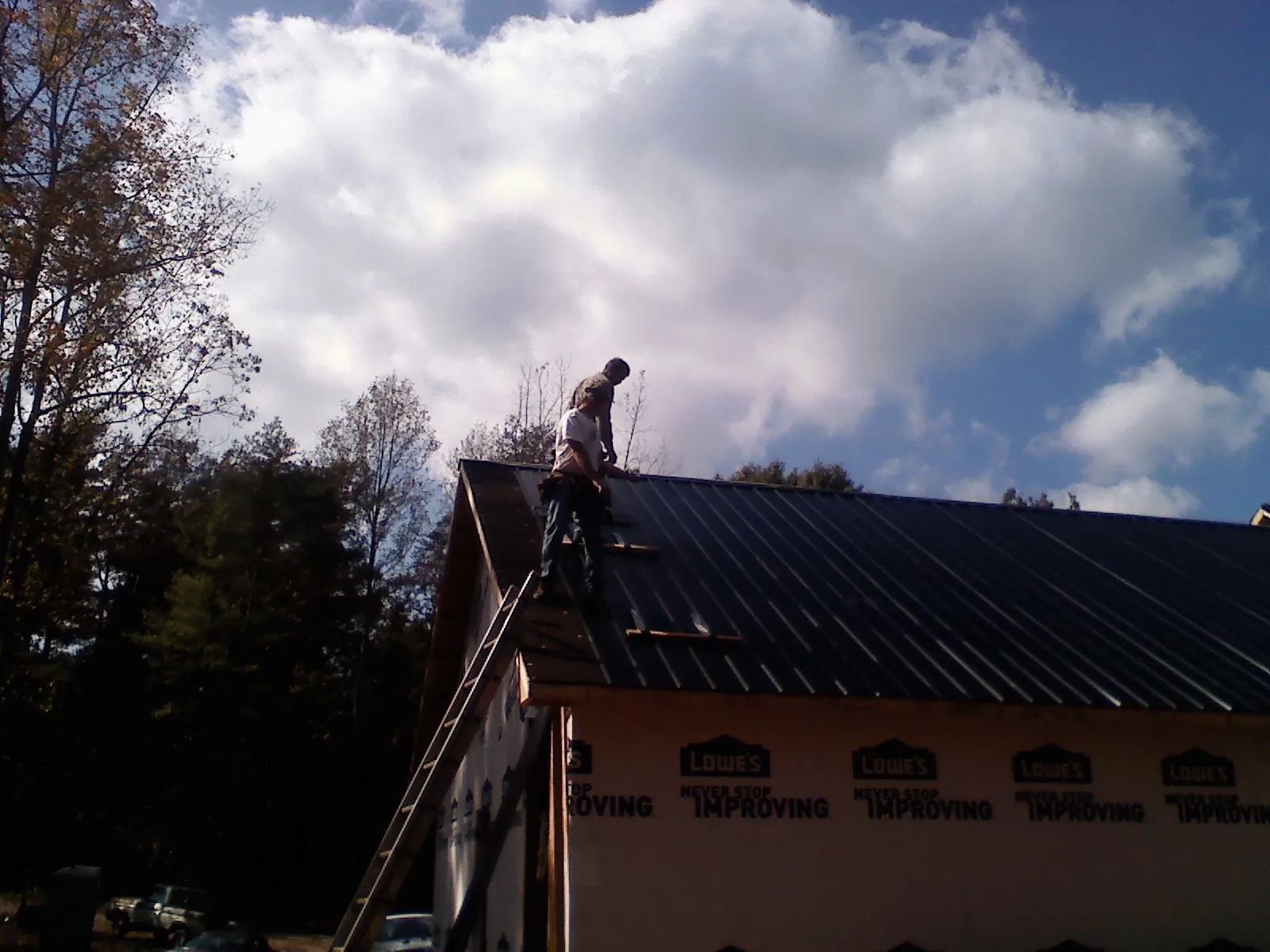 Roofer fastening dark metal panels high against a cloudy sky, from a Roof Inspection job in Saint George